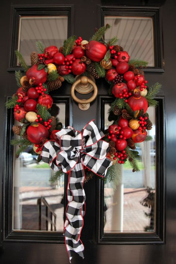 a bright fall wreath of faux fruit, berries, pinecones, evergreens and a large plaid bow on top