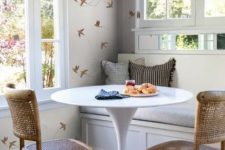 a cool and cozy dining area with a built-in bench, a round table, woven chairs, beautiful wallpaper and views
