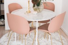 a cozy glam dining nook with a round table, pink chairs, a vase with blooms and a candle plus a fluffy rug is very cool