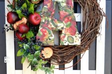 a farmhouse fall wreath of vine, appes and apple slices, berries, foliage, a bright paper mache monogram