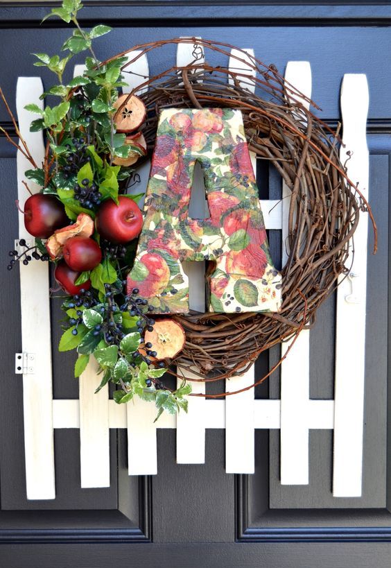 a farmhouse fall wreath of vine, appes and apple slices, berries, foliage, a bright paper mache monogram