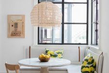 a light-filled dining area by the windows, with a built-in corner bench, a round table, a woven chair and a pendant lamp