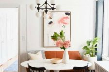 a lovely modern dining area with a rust-colored leather loveseat, printed textiles, a round table, black chairs, a modern chandelier