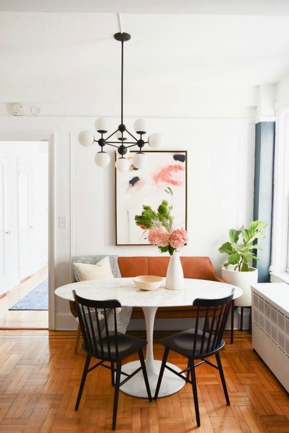 a lovely modern dining area with a rust-colored leather loveseat, printed textiles, a round table, black chairs, a modern chandelier
