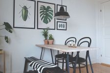 a lovely modern dining nook with a light stained table, a black bench and chairs, a small gallery wall with cool prints