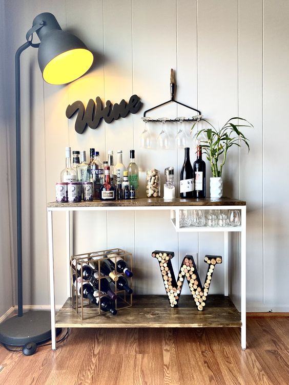 a lovely rustic home bar with a Vittsjo table redone with light-stained wood, with a sign, some bamboo, a wine bottle stand and a cool wine cork monogram