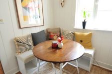a lovely small dining nook with a corner storage bench, colorful pillows, a round table, a bold artwork and a woven pendant lamp