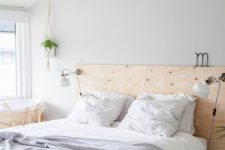 a neutral Nordic bedroom with a white bed with storage, a plywood headboard, IKEA Ranarp sconces that brign light