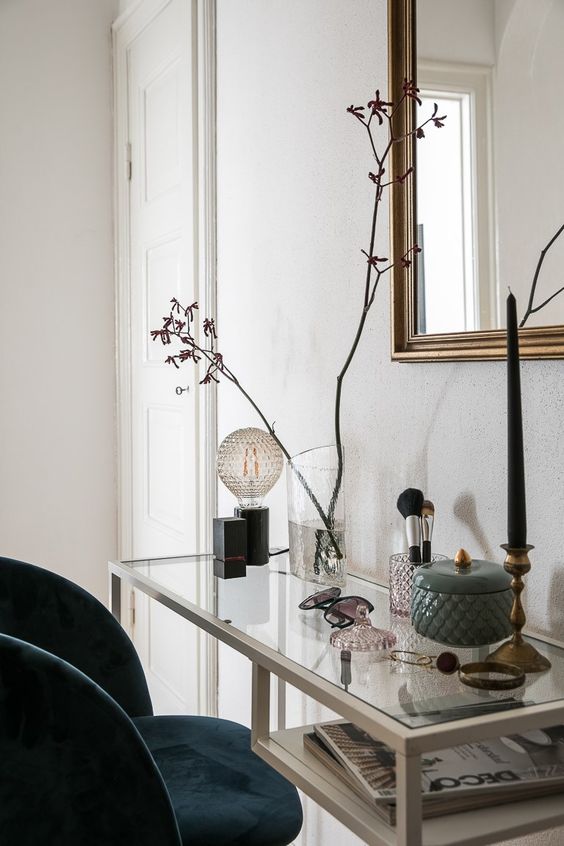 a refined and elegant vanity space wiht a white Vittsjo desk, a bulb, a candle, some accessories and makeup plus blooming branches is wow