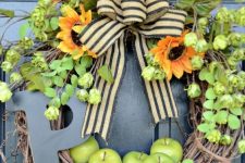 a rustic fall wreath of vine, foliage, greenery, bright blooms, apples, a striped bow and a large monogram