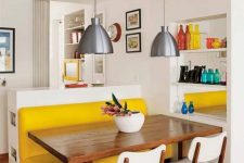 a small and bright dining space with a yellow upholstered bench, a stained table, white chairs, metal pendant lamps