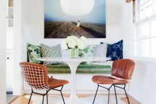 a small and colorful dining area with a built-in bench, a round table, leather chairs, a rug and a bold artwork