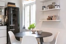 a small and cozy dining nook with open shelves, a round table, white chairs, a chic white pendant lamp