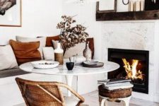 a small and cozy dining space with a fireplace, a round table, a built-in bench, a rattan chair and a leather stool