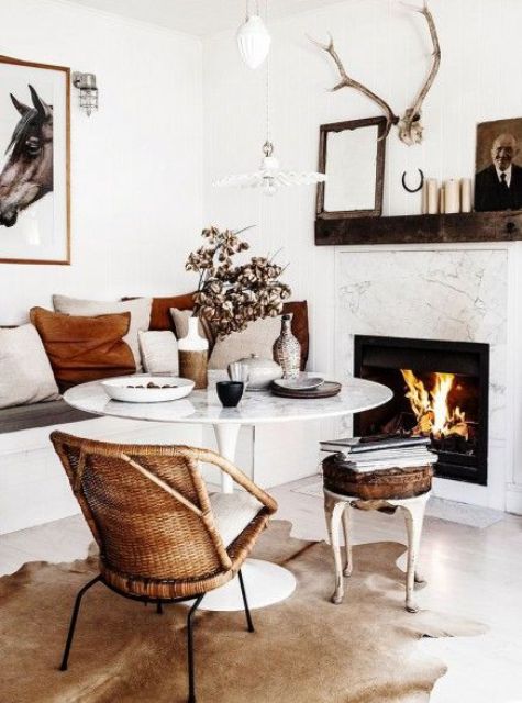 a small and cozy dining space with a fireplace, a round table, a built in bench, a rattan chair and a leather stool