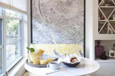 a small and cute dining nook with a colorful bench, a round table, a black chair, a pendant lamp and some yellow tableware