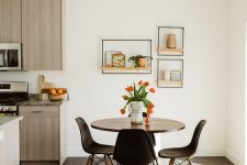 a small and lovely dining nook with a round table, black chairs, a woven rug and some open shelves with decor