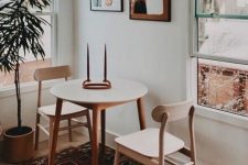 a small modern dining nook with a round table, wooden chairs, a pretty gallery wall, a potted plant and layered rugs