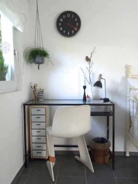 a small working space by the window with a black Vittsjo desk, a white chair, a small fire cabinet under the desk, a black clock and greenery