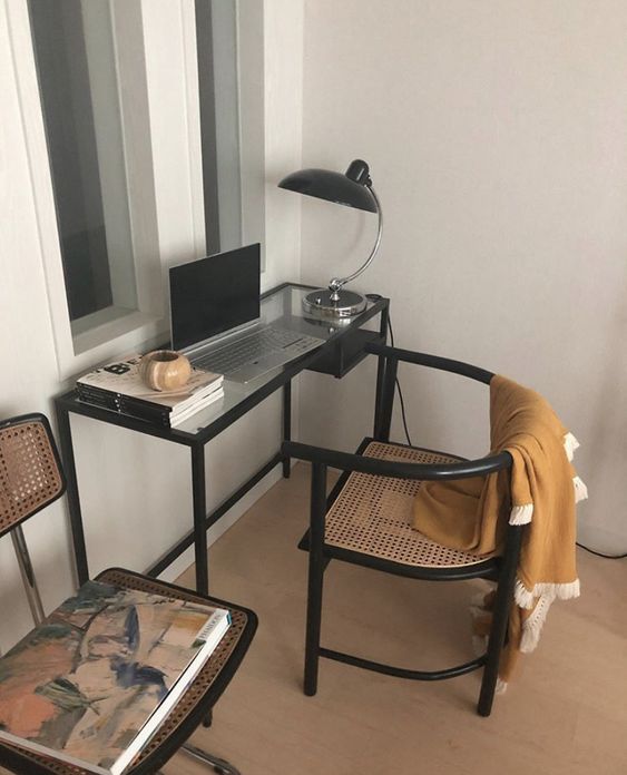 a stylish and cozy working space with a black Vittsjo desk and a black and cane chair, a black table lamp and some decor and books