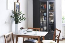 a stylish modern dining nook with a table, blue and green chairs, greenery in pots and vases and a gallery wall with clocks and plates