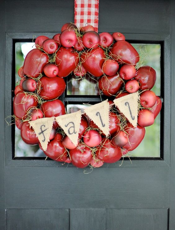 a super bold fall wreath of faux red apples, hay, a burlap banner and a plaid ribbon is cool for decorating your front door