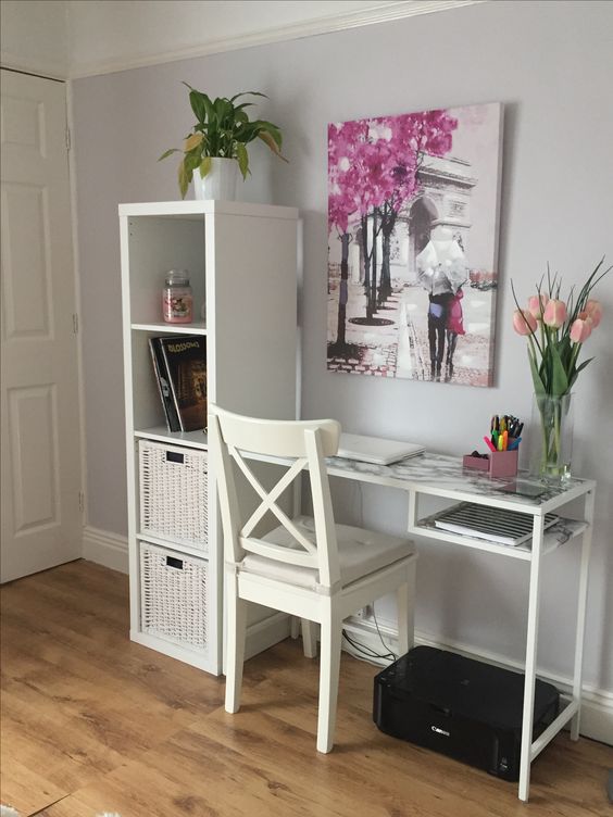 a working space with a white storage unit with crates, a white Vittsjo desk with a marble tabletop, a white chair, pink tulips and a bright artwork