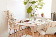 an airy small dining zone with a round table, stained and white chairs, potted plant, a hanging bulb and some printed textiles