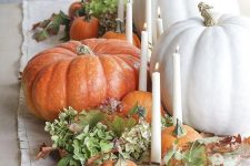 a beautiful and natural fall centerpiece of green blooms, fall leaves, gourds and pumpkins and thin and tall candles