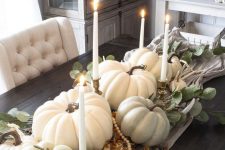 a beautiful fall centerpiece of faux pumpkins, wooden beads, antlers, greenery and elegant thin and tall candles