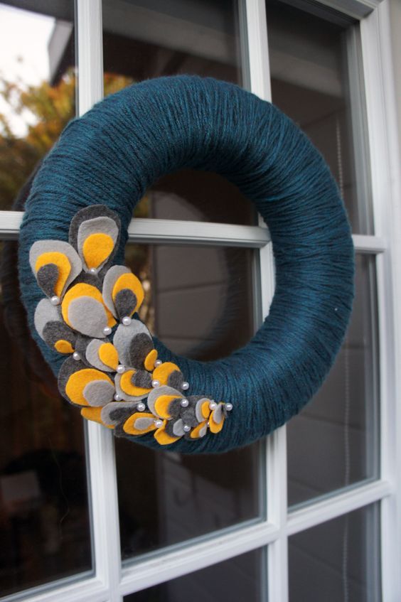 a bold fall wreath styled in non-typical colors, covered with navy yarn and with colroful fabric petals and pearls