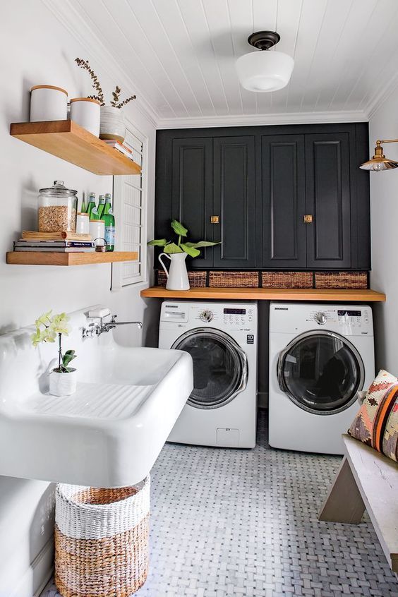 a bold modern laundry with a marble tile floor, black cabinets, a wooden countertop and a washing machine and a dryer, a sink and a basket