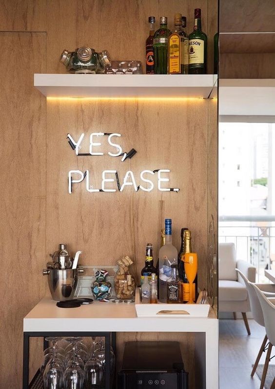 a chic modern home bar with a white bar with open storage, a lit up shelf and a neon sign