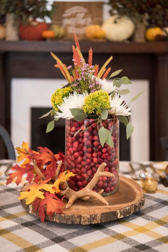 a chic woodland fall centerpiece of a wood slice, antlers, fall leaves, a glass with cranberries, blooms and leaves