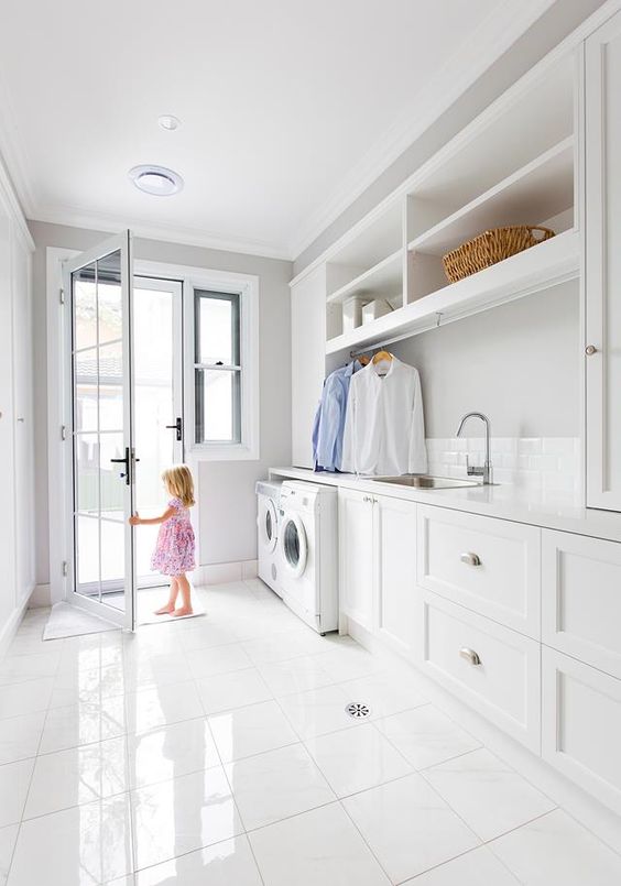 a clean and neutral laundry with shaker style cabinets, grey walls, open shelves, a washing machine and a dryer and a tiled floor