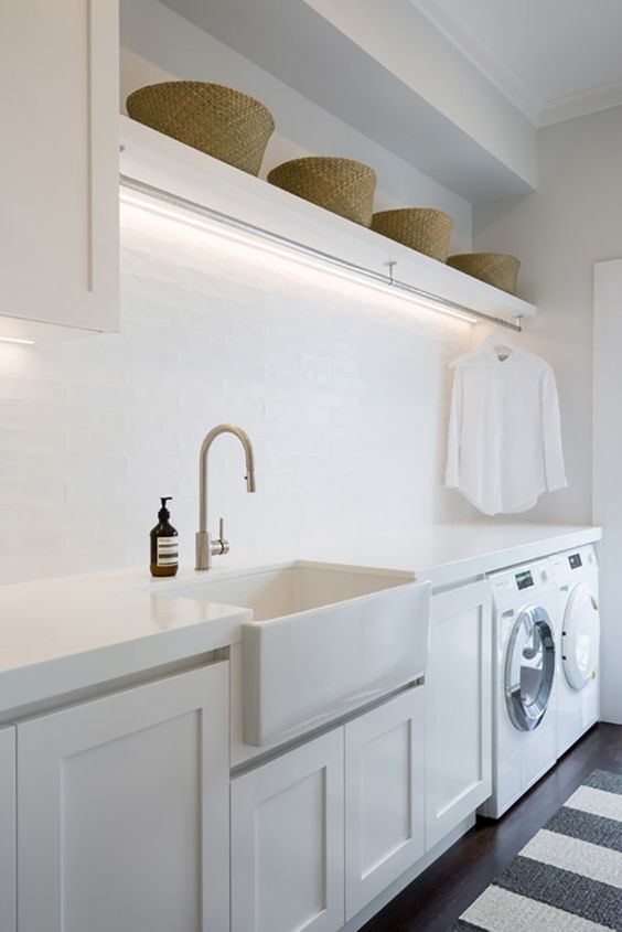 a clean neutral laundry room with white shaker style cabinets, white countertops, a square sink, baskets for storage and built-in lights