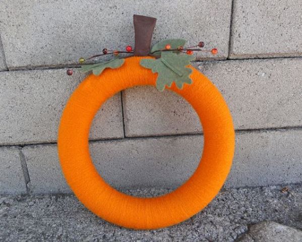 a colorful fall wreath covered with orange yarn, with fabric leaves and berries imitates a pumpkin