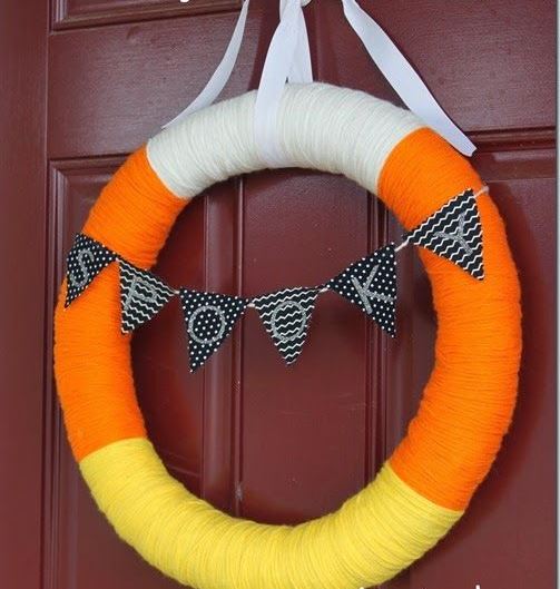 a colorful fall yarn wreath covered with white, orange and yellow yarn, with a black and white bunting for Halloween
