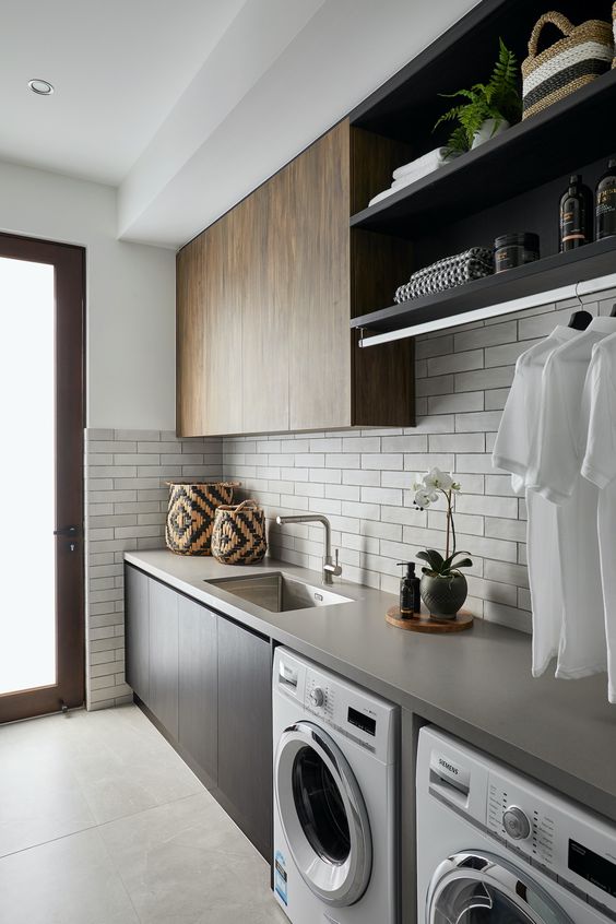 a contemporary laundry with sleek stained cabinets, a concrete countertop, neutral narrow tiles on the backsplash and a neutral floor