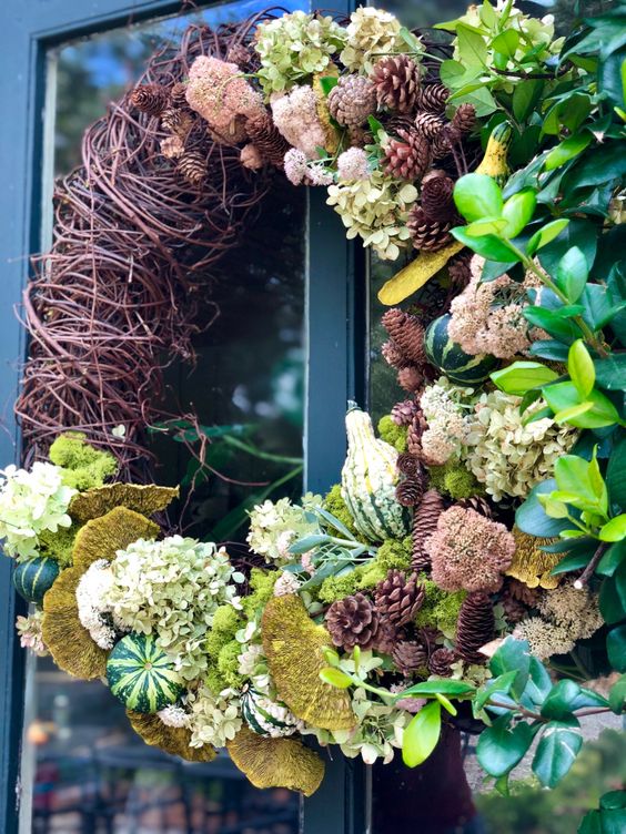 a creative fall wreath of white hydrangeas, vine, pinecones, greenery, gourds, mushrooms and greenery looks very eye-catchy