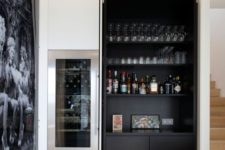 a dark built-in home bar with open shelves, artworks and sleek drawers is very stylish and chic