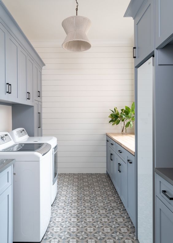 a dusty blue modern farmhouse laundry with shaker kitchen cabinets and black handles, printed tiles, a washing machine and a dryer