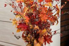 a fall centerpiece of a glass vase filled with nuts and acorns, with berry twigs and branches and fall leaves is very bright