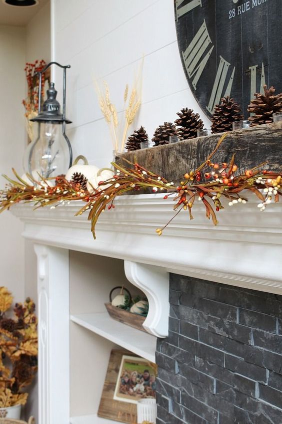a fall mantel with berry branches, white pumpkins and wheat and some pinecones on the rough wood mantel