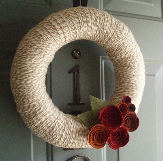 a fall wreath covered with neutral yarn, with moody burgundy fabric blooms and leaves