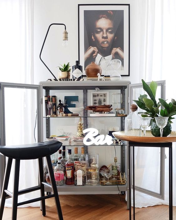 a glass bar cabinet with artworks, a lamp, some plants and a neon sign is a very chic idea