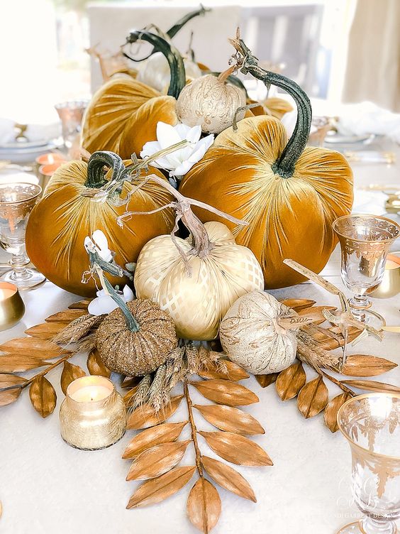 a golden fall centerpiece of mustard velvet pumpkins, dried leaves, white flowers and candles