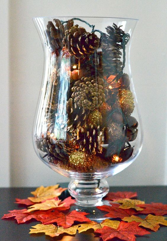 a large glass with gilded pinecones and lights is a great fall decoration or centerpiece to try