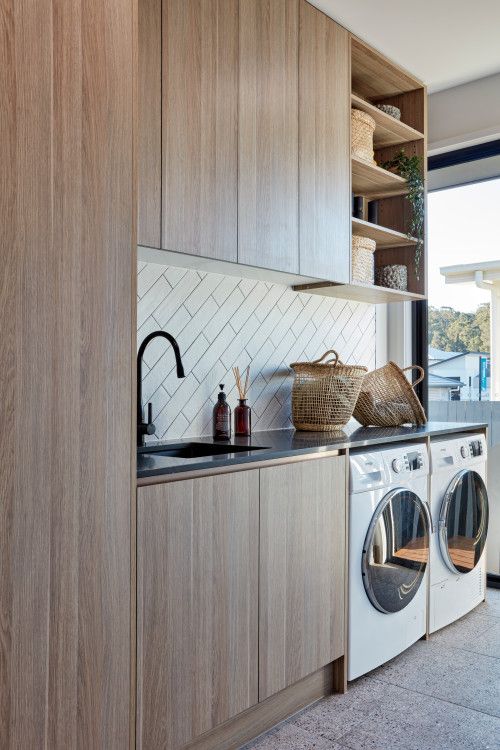 a lovely mid-century modern laundry with sleek stained cabinetry, a diagonal white tile backsplash, a black counertop and fixtures