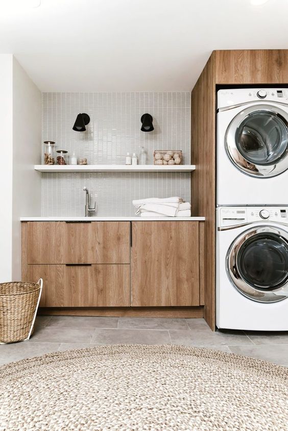 a mid-century modern laundry with sleek stained cabinets, a grey skinny tile backsplash, a jute rug and stacked appliances